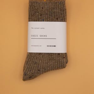 Puede incluir: Un par de calcetines marrones moteados con una etiqueta blanca que dice "The coziest socks, COZZZI SOCKS, cozziapparel.com".