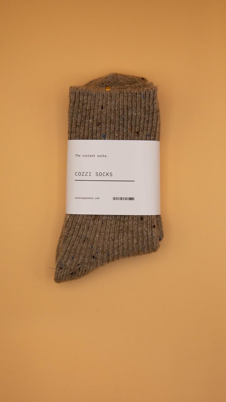 Puede incluir: Un par de calcetines marrones moteados con una etiqueta blanca que dice "The coziest socks, COZZZI SOCKS, cozziapparel.com".