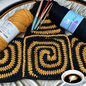 May include: A handmade crochet project in progress, featuring a black and gold spiral design. The image includes skeins of gold and black yarn, crochet hooks, and a cup of coffee with latte art. The yarn is labeled "Wool Thread".