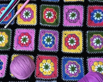 May include: A colorful, handmade crochet blanket featuring square motifs with floral designs in various colors, including yellow, pink, green, and blue. The blanket is displayed with crochet hooks, yarn, and scissors, suggesting a crafting project.