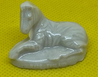 May include: A small, off-white ceramic figurine of a reclining horse. The horse is in a resting position, with its head raised and its legs tucked beneath its body. The base of the figurine reads "WADE ENGLAND".