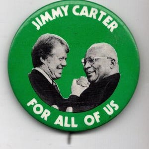 May include: A round green political campaign button featuring a black and white photograph of Jimmy Carter shaking hands with another individual. The text JIMMY CARTER is printed in white at the top, and FOR ALL OF US is printed in white at the bottom.