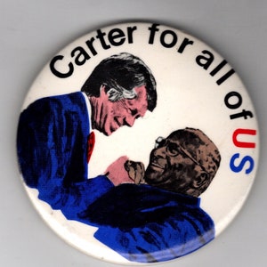 May include: A white button with a blue and red image of two men shaking hands. The text "Carter for all of us" is printed around the edge of the button.