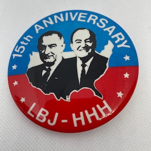May include: A red, white, and blue button with a black and white image of Lyndon B. Johnson and Hubert Humphrey. The button reads "15th Anniversary LBJ-HHH".
