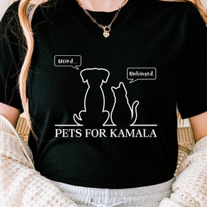 Puede incluir: Una camiseta negra con un gráfico blanco de un perro y un gato con burbujas de diálogo que dicen "Weird..." y "Unhinged". El texto "PETS FOR KAMALA" está debajo del gráfico.