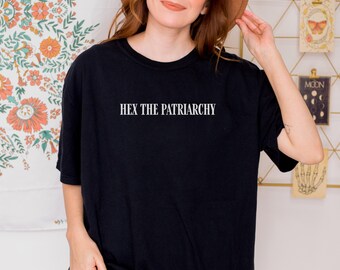 May include: Black t-shirt with the text "HEX THE PATRIARCHY" in white. The shirt is a basic crew neck style. The model is wearing a brown hat.