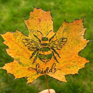 May include: A yellow maple leaf with a bee cutout and the word "kind" written below it.