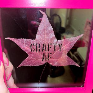May include: A framed leaf with the words "CRAFTY AVE" written on it. The frame is a bright pink color.