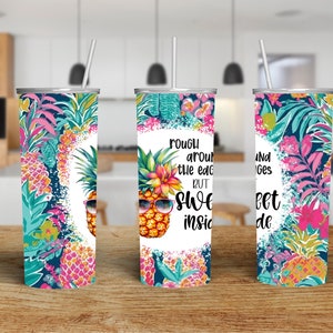 Może przedstawiać: Trzy kubki ze stali nierdzewnej z białym tłem i wzorem ananasa. Kubki mają tropikalny wzór kwiatowy i tekst "Szorstkie na krawędziach, ale słodkie w środku".