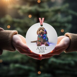 Round Christmas ornament with a labradoodle wrapped in colorful Christmas lights.  Axel and 2025 are at the bottom.  Name and year can be personalized.