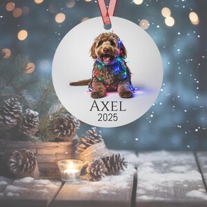 Round Christmas ornament with a labradoodle wrapped in colorful Christmas lights.  Axel and 2025 are at the bottom.  Name and year can be personalized.