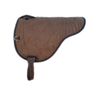 Puede incluir: Silla de montar acolchada marrón con ribete negro y una correa marrón con hebilla. La silla de montar tiene un anillo en el lateral.
