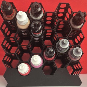 May include: Black hexagonal paint bottle organiser with 12 compartments, filled with various coloured bottles of paint.