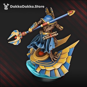 Peut inclure: Figurine détaillée d'Anubis, le dieu égyptien des morts, avec une tête de chacal et un sceptre. La figurine est peinte dans des tons de bleu, d'or et de marron. La base est en forme de bateau stylisé. Le texte "DakkaDakka.Store" est en haut à gauche.