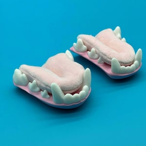 May include: Two whimsical, pink and white teeth-shaped objects. Each has a pink, textured center, surrounded by white, pointed teeth. The base is a light pink with a blue outline, set against a bright blue background.