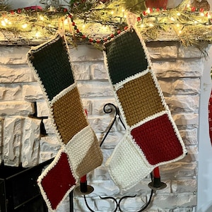 May include: Two crocheted Christmas stockings with a patchwork design. The stockings are green, brown, white, and red. They are hanging on a fireplace mantel.