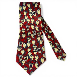 May include: A red necktie featuring a repeating pattern of the Tasmanian Devil cartoon character in various poses. The tie has a classic shape and is made of a smooth fabric. The cartoon character is in shades of yellow, gray, and white.