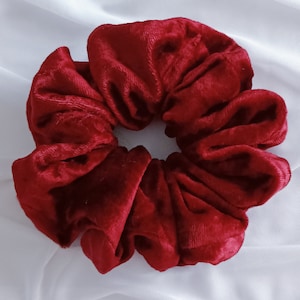 May include: A red velvet scrunchie hair tie. The scrunchie is made of soft, plush velvet and is a popular hair accessory.