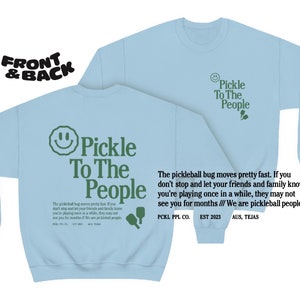 Puede incluir: Sudadera azul claro con una cara sonriente verde y el texto "Pickle To The People" en la parte delantera. La parte posterior de la sudadera tiene el mismo texto y un gr&aacute;fico de pala verde. El texto "The pickleball bug moves pretty fast. If you don't stop and let your friends and family know you're playing once in a while, they may not see you for months /// We are pickleball people." est&aacute; impreso en la parte posterior. El texto "PCKL PPL CO. EST 2023 AUS, TEJAS" tambi&eacute;n est&aacute; impreso en la parte posterior.