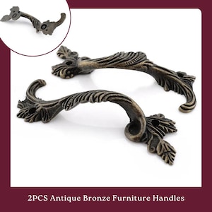 May include: Two antique bronze furniture handles with a decorative floral design. The handles are about 4 inches long and have a curved shape.