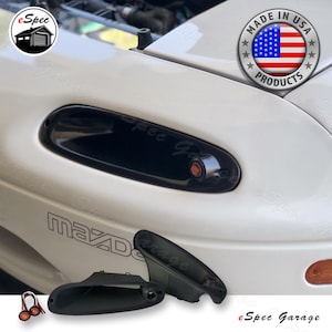 May include: Black automotive turn signal light housing and lens, with the text "eSpec Garage" and "Made in USA Products". The image shows a white car with the Mazda logo.