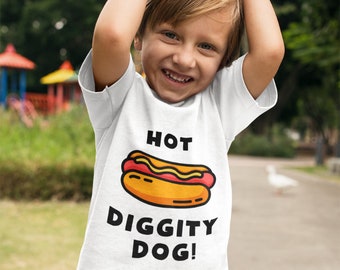 May include: A white t-shirt featuring a cartoon hot dog and the words "HOT DIGGITY DOG!". The hot dog illustration is yellow, red, and orange. The shirt is worn by a child.