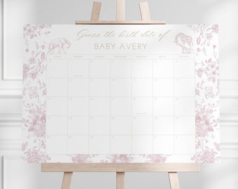 May include: A white calendar with a pink floral border and the text "Guess the birth date of BABY AVERY." The calendar features illustrations of an elephant, giraffe, and teddy bear. It is displayed on a wooden easel.