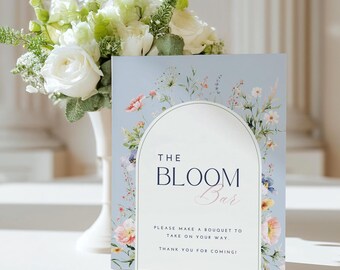 May include: A blue and white floral sign with the text "THE BLOOM Bar" and the instructions "PLEASE MAKE A BOUQUET TO TAKE ON YOUR WAY. THANK YOU FOR COMING!"