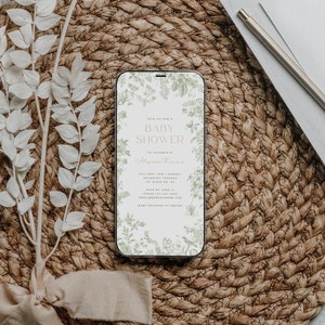 May include: A digital invitation on a smartphone screen for a baby shower. The invitation features a floral design with green leaves and white flowers. The text reads "Join us for a Baby Shower to celebrate Alysa Thomas. July 3rd | 3pm | Sunday Roundtop Terrace 1st Ridge Rd. NY RSVP by June 11 Sarah 123-456-7890 email@babyshower.com Baby Registry at Period"