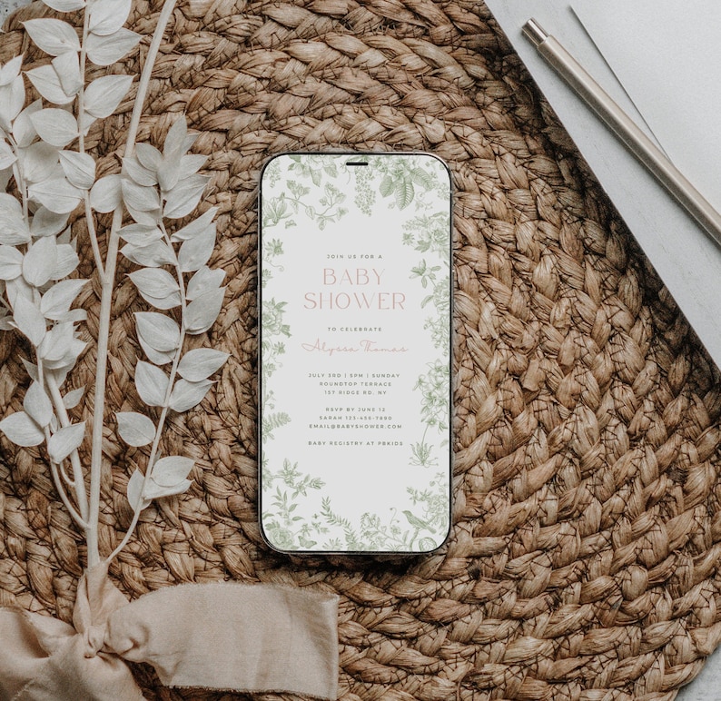 May include: A digital invitation on a smartphone screen for a baby shower. The invitation features a floral design with green leaves and white flowers. The text reads "Join us for a Baby Shower to celebrate Alysa Thomas. July 3rd | 3pm | Sunday Roundtop Terrace 1st Ridge Rd. NY RSVP by June 11 Sarah 123-456-7890 email@babyshower.com Baby Registry at Period"