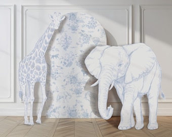 May include: A tall giraffe cutout and a large elephant cutout stand in front of an arched panel featuring a blue and white toile de jouy pattern with various animal illustrations, including a hot air balloon and floral motifs.