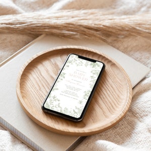 May include: A smartphone displaying a baby shower invitation with a floral design. The invitation reads "Join us for a Baby Shower in celebration of [Name]" and includes the date, time, and location of the event.