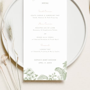 May include: A menu for a baby shower with a safari theme. The menu features a first course of goat cheese and eggplant tart, a main course of roasted leg of lamb or penne alla vodka, and a dessert of lemon tart. The menu is decorated with a green floral border.
