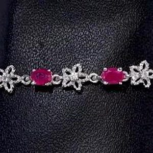 Op de afbeelding: Een zilveren armband met rode ovale edelstenen en bloemmotieven. De armband heeft een delicaat kettingontwerp.