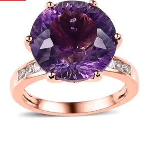 Pode incluir: Um anel de ouro rosa com uma grande ametista redonda de cor púrpura rodeada por uma banda de diamantes pequenos e transparentes.