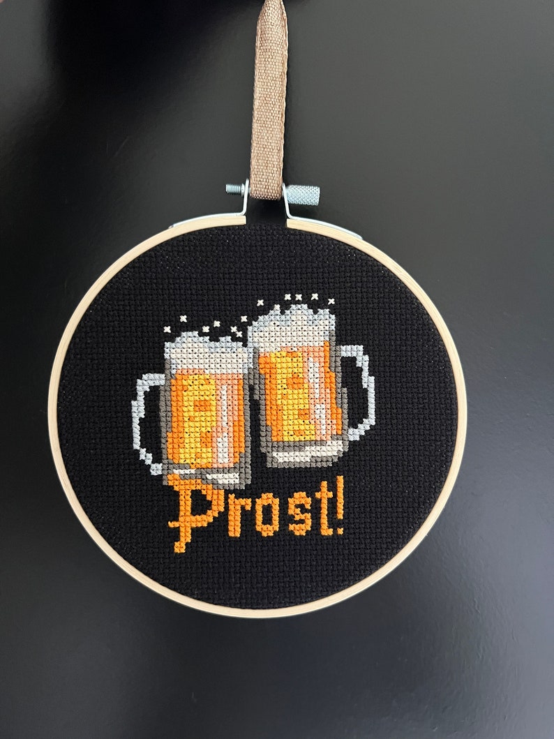 May include: A black embroidery hoop with a cross-stitch design of two beer steins and the word "Prost!" in yellow thread.