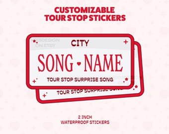 May include: Customizable tour stop stickers. The stickers are rectangular with a red border and white background. The text "CITY", "SONG-NAME", and "TOUR STOP SURPRISE SONG" are displayed. The stickers are 2 inches in size and waterproof.