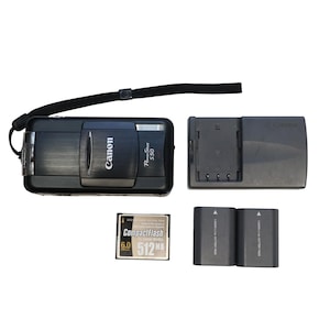 May include: A black Canon PowerShot S50 digital camera with a wrist strap, charger, two batteries, and a CompactFlash card. The camera has the Canon logo and model name on the front.
