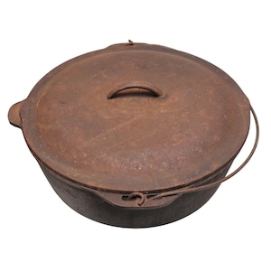 May include: A rusty cast iron Dutch oven with a lid and a wire handle. The pot is round with a lid that has a small handle. The Dutch oven is designed for cooking and has a rustic appearance.