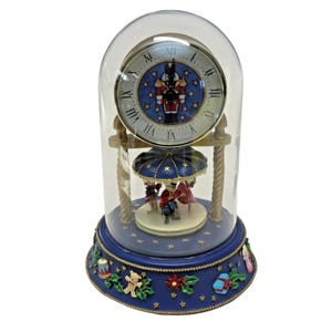 May include: A decorative blue and gold carousel clock with a glass dome. The clock face features Roman numerals and a nutcracker design. The base is adorned with festive holiday decorations.