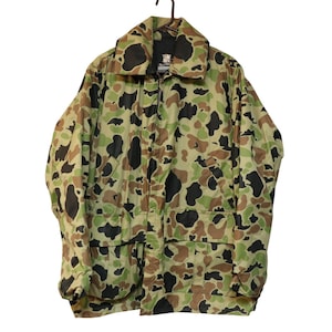 Puede incluir: Una chaqueta de camuflaje verde, marrón y negro con cierre de cremallera y dos bolsillos grandes en la parte delantera.