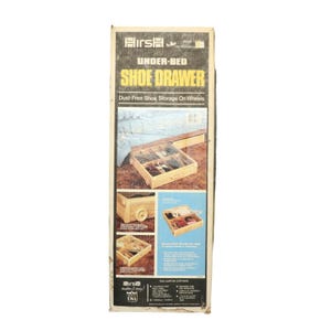 May include: A rectangular cardboard box for a Hirsh Under-Bed Shoe Drawer. The packaging features yellow and white text on a black background, displaying images of a light-colored wooden storage drawer with wheels and internal dividers.