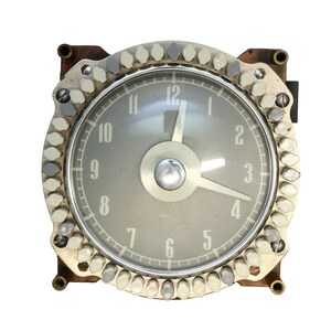 May include: A vintage circular analog clock with a grey face, white numerals from 1 to 12, and two silver hands. The clock is encased in a square metal frame surrounded by a ring of small, alternating white and grey plastic push-button switches.