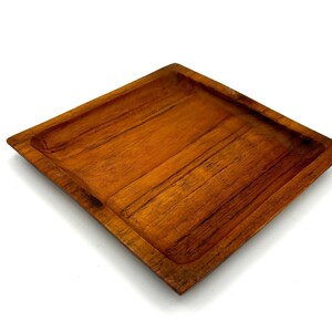 May include: A square wooden serving tray with a natural wood finish. The tray has a slightly raised edge and is made of solid wood.
