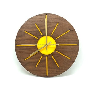 May include: A round wooden clock with a yellow sunburst design. The clock has gold-coloured hands and a yellow centre.