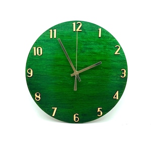 May include: A green wooden clock with gold-colored numbers and hands. The clock face has a wood grain pattern.