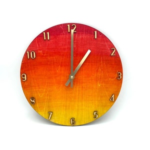 May include: A wooden clock with a red, orange, and yellow gradient design. The clock face has black Roman numeral hour markers and black hands.