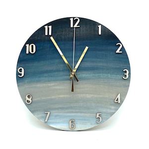 May include: A round, blue and white ombre clock with gold hands and silver numbers. The clock face has a gradient of blue shades, fading to white at the bottom.
