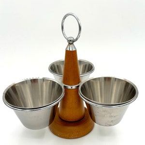 May include: A wooden condiment holder with three stainless steel bowls. The holder has a cone-shaped base with a ring handle on top.