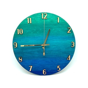 May include: A round wooden clock with a blue and green ombre design. The clock face has gold numbers and hands.